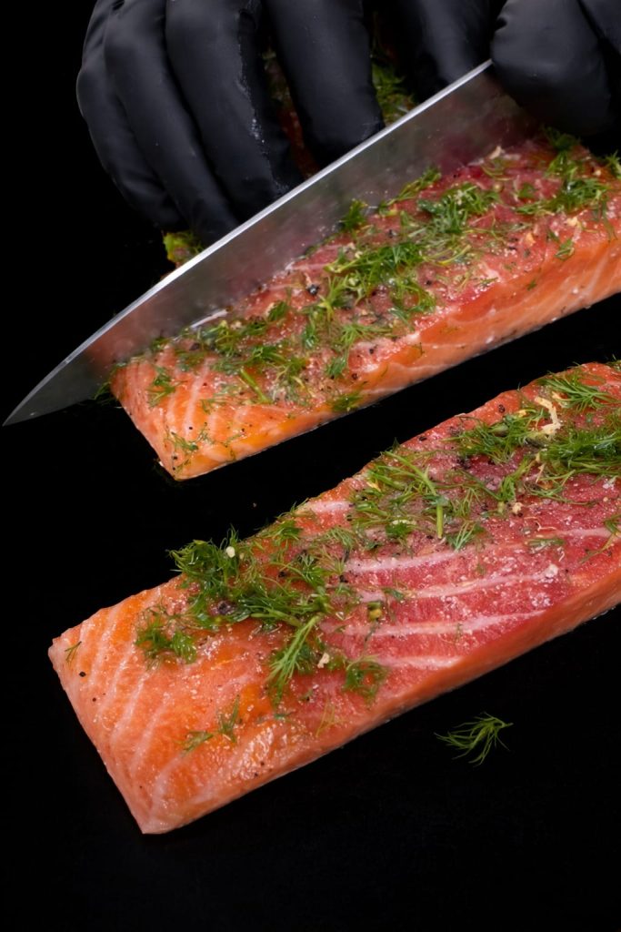Private chef seasoning fresh salmon fillets with dill, menu preparation for a private dining stay