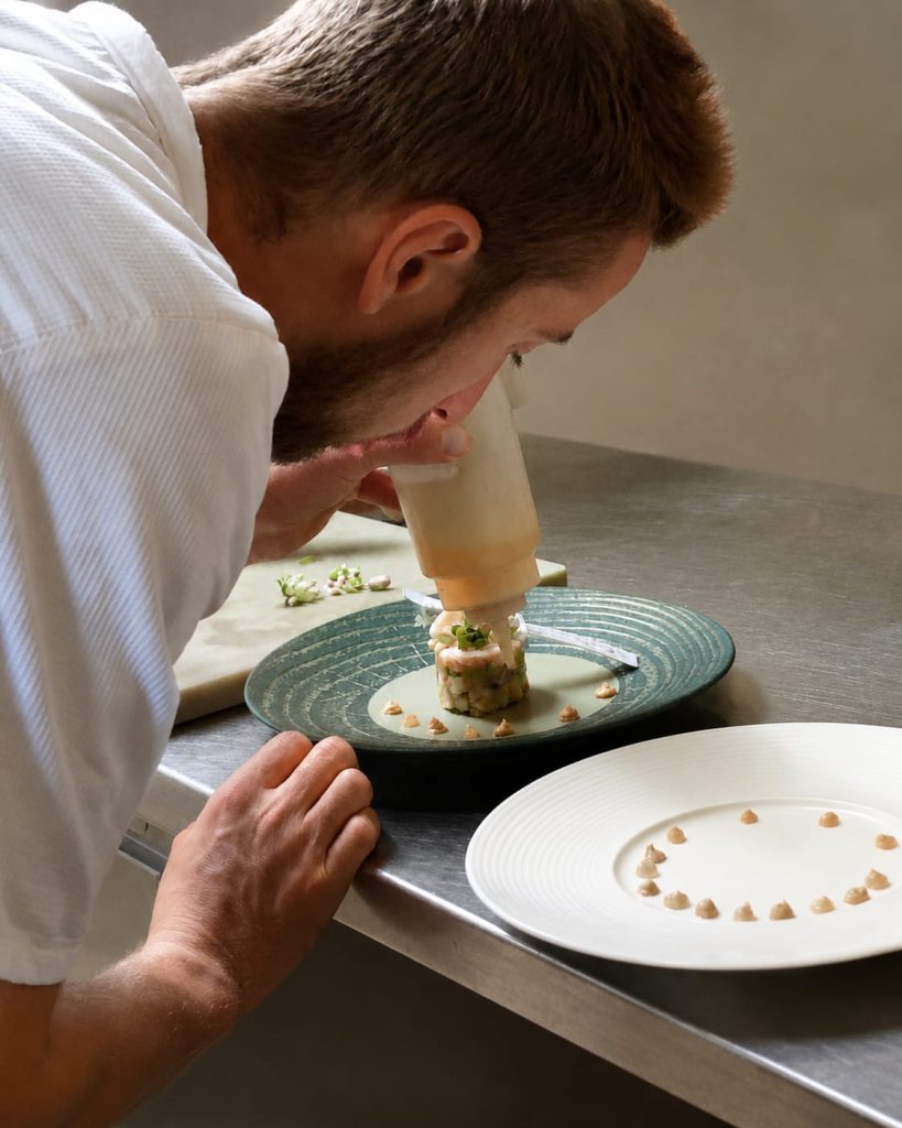 Private chef plating a dish with precision in a chalet kitchen, discreet on-site dining service